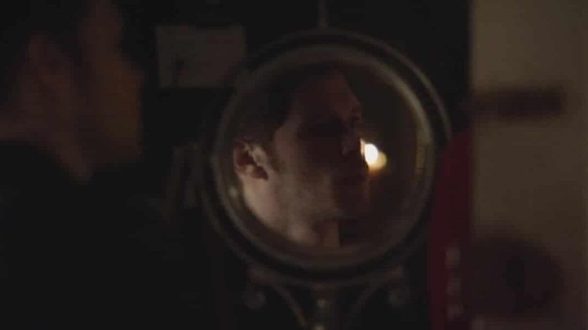 Klaus in front of mirror looking back at Camille.