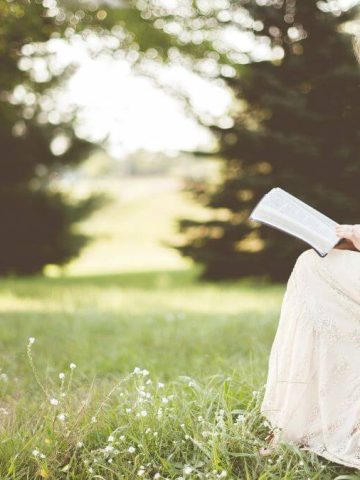 girl reading book outside and sitting on a large stone